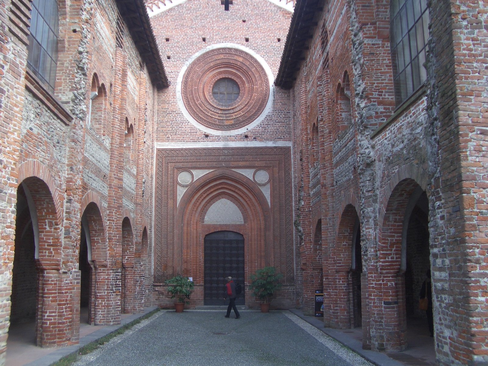 Fachada de ladrillo y rosetón de la abadía de los Santos Nazario y Celso, vista entre las alas del antiguo nartece. Foto: Laurom, fecha declarada 2007; Wikimedia Commons.